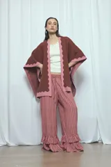 Poncho marrón con detalles de bordes ondulados en color rosado, confeccionado en mezcla de acrílico, poliéster y elastano, de diseño abierto y mangas amplias.