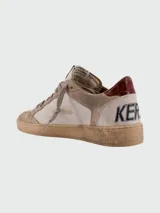 Zapatillas deportivas Golden Goose modelo Ball Star, estilo vintage y desgastado. Combinan paneles de cuero y gamuza en tonos beige y topo, con estrella lateral en azul marino y talón en cuero burdeos. Presentan escritura a mano en la suela.