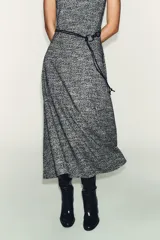 Vestido midi sin mangas, con cuello perkins y cierre de cremallera oculta en la espalda. Presenta un tejido con textura en blanco y negro, y un cinturón fino de efecto piel con anilla metálica. La falda tiene un corte evasé.