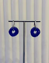 Aros tipo argolla con dije de vidrio en forma de dona color azul intenso, montados sobre una estructura de plata 925.