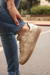 Zapatilla urbana de cuero color dorado, con cordones y suela marrón.