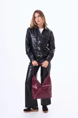 Bolso tipo hobo de cuero sintético negro con acabado brillante, decorado con tachuelas plateadas a lo largo de la correa y en el borde frontal. Presenta un diseño asimétrico en la parte superior.