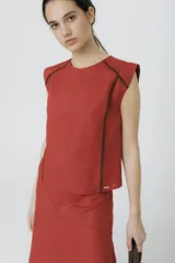 Blusa sin mangas color terracota, con cuello redondo y vivos de color marrón oscuro que recorren los hombros y los laterales del torso.