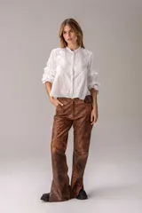 Camisa blanca de estilo romántico confeccionada en tela bordada con detalles de calados y volados en las mangas. Presenta cuello alto con terminación fruncida, cierre frontal con botones y diseño de alforzas verticales en el frente.