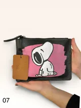 Sobre de cuero marrón con diseño pintado a mano que presenta al personaje Snoopy sobre un fondo rosado y la palabra 'heal'. Cuenta con cierre superior y etiqueta de cuero colgante.