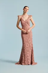 Vestido largo de fiesta de encaje color rosado, con escote en V, tirantes finos decorados con plumas y pedrería, y una sutil falda sirena con pequeña cola.