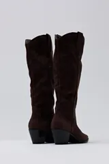 Bota de caña alta confeccionada en gamuza color chocolate, con diseño de estilo western, punta fina y taco cuadrado de altura media.