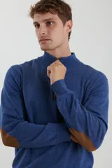 Sweater de punto gris con medio cierre frontal, cuello alto y coderas en tono marrón. Presenta un diseño clásico con puños y ruedo acanalados.