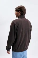 Buzo de polar color marrón con cuello alto y cierre frontal parcial. Presenta un bolsillo frontal tipo canguro y un estampado pequeño en el pecho con el texto 'NORTHERN ADVENTURES'. Cuenta con puños elásticos.