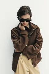 Chaqueta de tejido efecto ante color marrón, con cuello alto, cierre frontal con cremallera y botones a presión, manga larga y bolsillos de plastrón con solapa en el delantero.