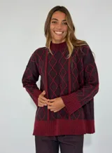 Sweater de lana color bordó con cuello alto y diseño de rombos y líneas verticales en rojo. Tiene puños y dobladillo acanalados.