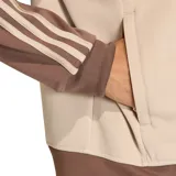 Campera deportiva Adidas SST Loose Tracktop, color beige con mangas y cuello marrón. Presenta las tres rayas características de Adidas en las mangas y el logo bordado en el pecho.