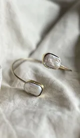 Pulsera rígida abierta de bronce dorado con dos perlas barrocas rectangulares en los extremos.