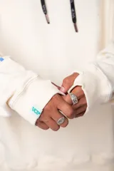 Buzo canguro amarillo ocre oversize de algodón rústico con capucha, cordones negros con letras blancas, bolsillo frontal y puños y cintura acanalados. Presenta estampados en el frente y las mangas.