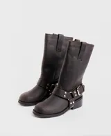 Bota de caña media confeccionada en cuero vacuno color marrón oscuro, con diseño de estilo biker. Presenta una tira decorativa con hebilla metálica y estribo desmontable en la zona del tobillo, taco cuadrado de madera y suela de caucho.