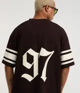 Remera deportiva de algodón color marrón con cuello en V y mangas cortas. Diseño overboxy con estampado de fútbol americano, lettering y rayas contrastantes en blanco.