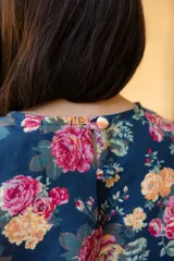 Vestido corto sin mangas de corte recto y holgado, confeccionado en lino con estampado floral multicolor sobre fondo azul oscuro. Presenta cuello redondo y cierre posterior con botones forrados.