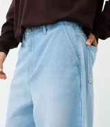 Pantalón de jean corte baggy, de tiro alto y pierna ancha, con diseño de cinco bolsillos, trabillas para cinturón y cierre frontal con botón y cremallera.