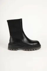 Bota corta negra de símil cuero, con punta redonda, laterales elastizados y suela tipo tractor de 5 cm de alto.
