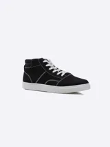 Bota de lona estilo urbano, color negro con costuras blancas visibles, cordones blancos y suela de goma blanca.