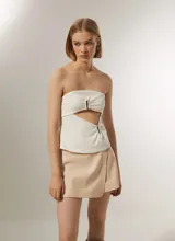 Top strapless color blanco, con diseño cut-out frontal y detalle de aros metálicos en el centro. Presenta un ajuste al cuerpo y cierre posterior.