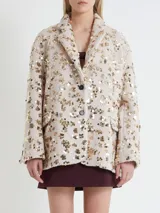 Blazer color crudo con lentejuelas doradas, de corte recto, con solapas de muesca, cierre con dos botones y bolsillos delanteros.