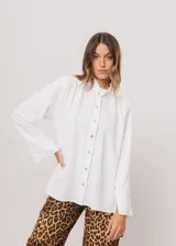 Camisa blanca de cuello redondo con frunces, abotonada y de manga larga con puño abierto.