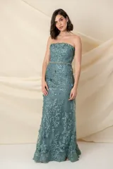 Vestido largo de fiesta color verde agua, confeccionado en tul bordado con apliques florales. Diseño strapless con escote asimétrico y capa de tul bordado sobre un hombro. Incluye cinto con strass y piedras. Ideal para madrinas o madres de quinceañeras.