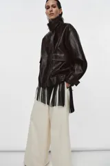 Chaqueta de cuero sintético con textura rugosa, cuello alto con trabilla, cierre frontal con cremallera y botones a presión, bolsillos delanteros y bajo ajustable con hebilla metálica.
