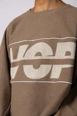 Buzo oversize de corte boxy, confeccionado en algodón rústico de alto gramaje en color beige. Presenta cuello redondo con borde crudo, mangas largas y una estampa frontal con el texto VCP delimitado por líneas horizontales blancas.