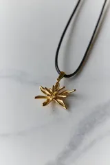 Collar con dije de acero quirúrgico en forma de flor de lirio, montado sobre un tiento de cuero encerado largo.