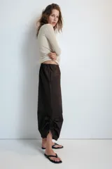 Pantalón culotte de tiro medio, color verde militar, con cintura elástica y bolsillos laterales ocultos. Presenta un diseño de bajo ancho con aberturas ajustables mediante cordones fruncidos en los laterales.