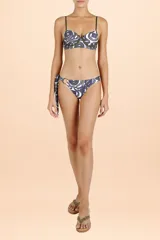Bombacha de bikini con diseño asimétrico, presenta un detalle de argolla circular en uno de los laterales y tiras para anudar. Posee un estampado orgánico en tonos verde oscuro y azul sobre fondo blanco.