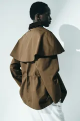 Chaqueta de sarga color marrón con cuello de pana de algodón oscura, capa decorativa desmontable, cierre de botones delanteros, bolsillos con solapa y cordón interior para ajustar la cintura.