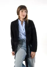 Blazer de gamuza negra con solapas clásicas, cierre frontal con botones y detalle de flecos en el ruedo. Cuenta con bolsillos laterales.