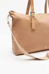 Cartera tipo tote de nylon negro, con diseño amplio y liviano. Presenta asas superiores fijas con detalles de tiras regulables y herrajes metálicos dorados. Incluye cierre principal y un pequeño logo metálico en la parte inferior frontal.