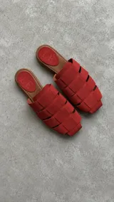 Zuecos de punta cuadrada, confeccionados en gamuza de color rojo, con diseño de tiras entrelazadas y plantilla marrón con el logo grabado.
