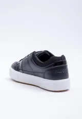 Zapatillas urbanas negras con detalle charol en el lateral y suela blanca.