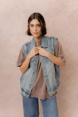Chaleco de jean con diseño oversized y lavado vintage. Presenta cuello camisero, cierre frontal con botones metálicos, bolsillos superiores con tapa y botón, bolsillos laterales y terminaciones desflecadas en las sisas.