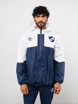 Campera de lluvia Umbro del Club Nacional de Football, con diseño de bloques de color en blanco y azul marino, detalles en rojo, capucha integrada y cierre frontal completo.