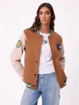 Campera estilo varsity con cuerpo en color marrón y mangas en tono beige. Presenta cierre frontal con botones a presión, cuello, puños y ruedo con franjas tejidas en verde y blanco. Incluye un parche con la letra R en el pecho y detalles bordados en las mangas.