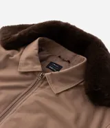 Campera bomber de sarga color tostado con cuello desmontable de pelo sintético oscuro. Presenta cierre frontal de cremallera, puños y cintura acanalados, y bolsillos laterales.