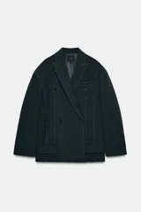 Blazer oversize de corte recto con cuello de solapa, manga larga con hombreras y cierre frontal de doble botonadura. Presenta un diseño en color gris oscuro con costuras decorativas a contraste en color blanco, bolsillos con solapa y forro interior.