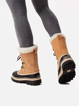 Bota de nieve Sorel modelo Caribou, con diseño impermeable de caña media. Presenta una parte superior de nubuck color tostado con cordones negros, base de goma vulcanizada negra y borde de pelo sintético en la parte superior.