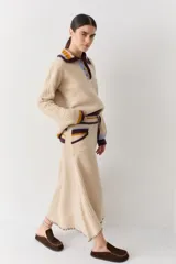 Falda midi de lana en color marrón, con diseño acampanado y tejido acanalado. Presenta una cintura elástica con cordón de ajuste, detalles de rayas en tonos beige y blanco en la parte superior, y costuras decorativas en el ruedo.