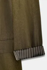 Blazer de lino color verde militar, con cuello solapa, hombreras y manga larga con puño revuelto con detalle a rayas. Cuenta con cierre frontal de un botón y bolsillos delanteros con solapa.