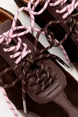 Zapatilla de cuero marrón con paneles de gamuza y cuero liso, suela de goma color caramelo y cordones bicolores en rosa y blanco.