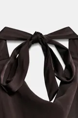 Top satinado negro de cuello halter drapeado con espalda descubierta y bajo asimétrico. Cuenta con cierre en la espalda y cuello con lazada.