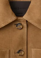 Chaqueta de ante color marrón claro, de diseño corto y recto, con cuello camisero, manga larga, dos bolsillos de parche delanteros y cierre frontal con botones.