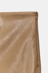 Falda midi de tiro medio confeccionada en tejido efecto piel de color marrón, con costura central frontal y cierre lateral con cremallera oculta.